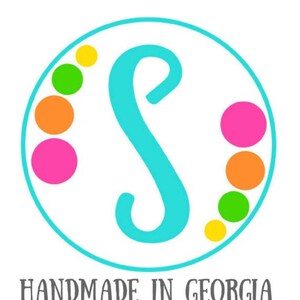 May include: A turquoise letter S in a white circle with a border of yellow, green, orange, and pink dots. The text "HANDMADE IN GEORGIA" is below the circle.