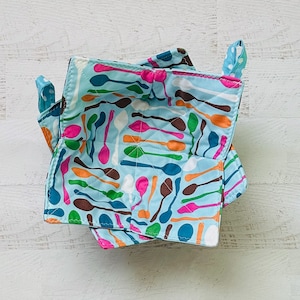 May include: A blue quilted fabric bowl with a spoon pattern. The bowl is folded and ready to be used.