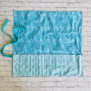 May include: A blue and white fabric pencil roll with a teal ribbon. The roll has a pocket with a green and white polka dot pattern.