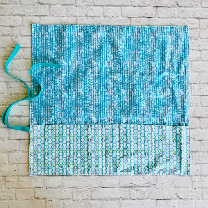 May include: A blue and white fabric pencil roll with a teal ribbon. The roll has a pocket with a green and white polka dot pattern.
