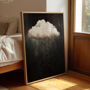 May include: A framed art print featuring a cloud with rain against a dark background. The cloud is white and fluffy, with rain falling in vertical lines. The artwork is in a wooden frame and leans against a wall.