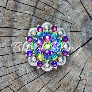 Pode incluir: Uma pe&ccedil;a redonda prateada com um design floral. O centro &eacute; preenchido com strass iridescentes em tons de roxo, azul, verde e rosa.