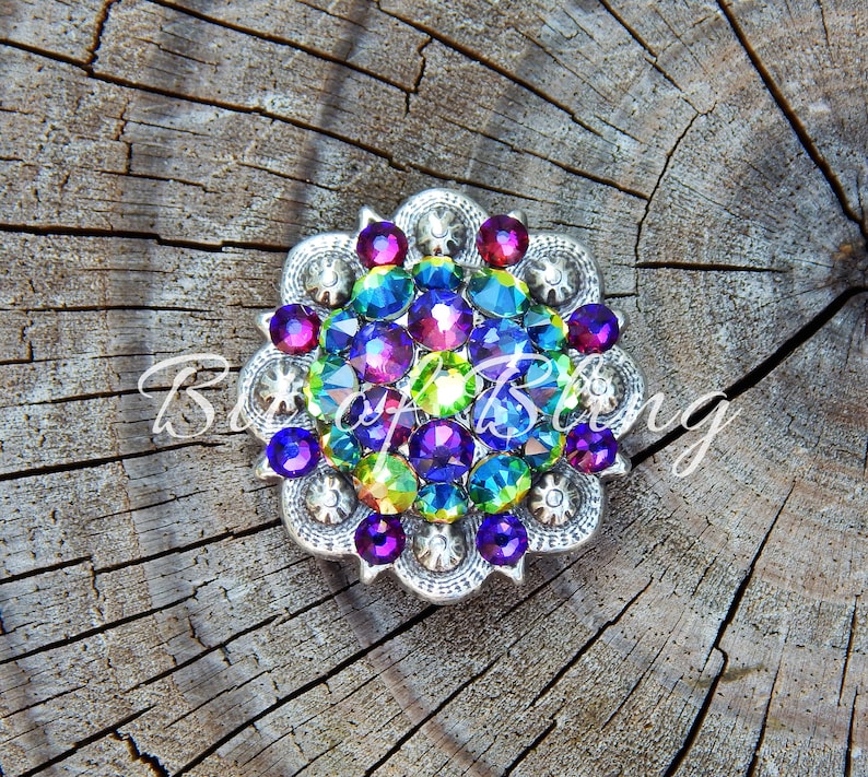 Pode incluir: Uma pe&ccedil;a redonda prateada com um design floral. O centro &eacute; preenchido com strass iridescentes em tons de roxo, azul, verde e rosa.