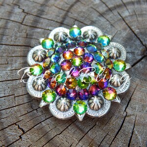 Pode incluir: Uma fivela redonda decorativa de cor prateada com um design floral. A fivela &eacute; adornada com uma variedade de pedras de imita&ccedil;&atilde;o iridiscentes em tons de verde, azul, roxo, laranja e vermelho.