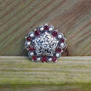 May include: Silver-toned concho with a floral design and red rhinestones.