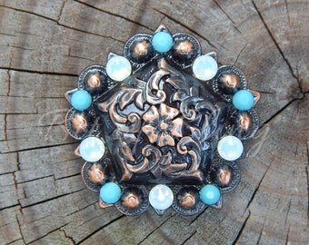 Könnte beinhalten: Dekoratives Metallornament in Bronzefarbe mit zentralem Blumendesign und einem Rand aus türkisfarbenen und weißen irisierenden Perlen. Das Ornament befindet sich auf einem rustikalen Holzgrund.