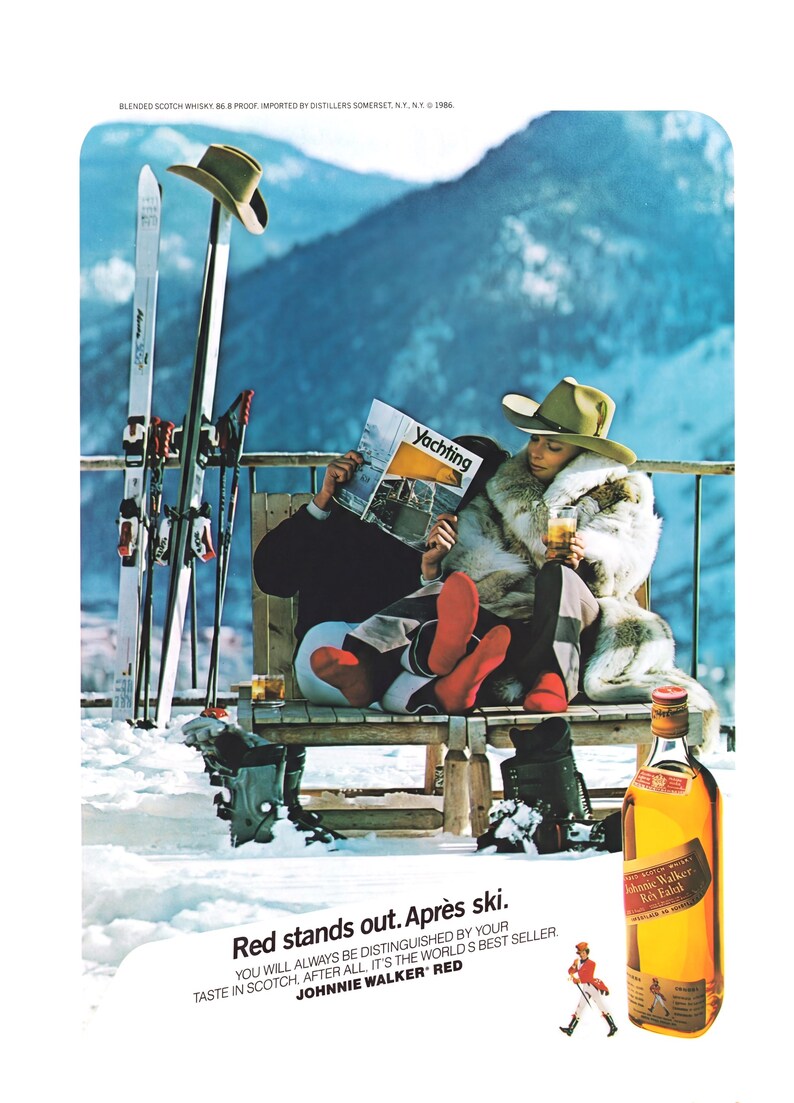Op de afbeelding: Vintage advertentie voor Johnnie Walker Red Label whisky. De sc&egrave;ne toont een stel na het ski&euml;n, met ski's en laarzen. De tekst luidt "Red stands out. Apr&egrave;s ski" en de merknaam.