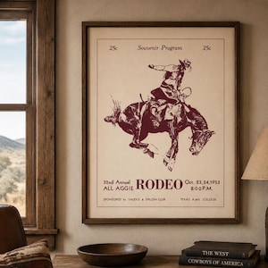 Puede incluir: Un póster enmarcado de estilo vintage con una ilustración de color rojo oscuro de un vaquero montando un caballo que corcovea. El texto dice: 25c Souvenir Program, 32nd Annual All Aggie RODEO, Oct. 23, 24, 1953, 8:00 P.M., Sponsored by Saddle & Sirloin Club, Texas A&M College.