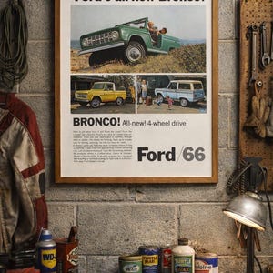 May include: A framed vintage advertisement for the Ford Bronco, featuring a green, yellow, and blue Bronco. The ad includes the text "Ford's all-new Bronco!" and "BRONCO! All-new! 4-wheel drive!" The image is set in a garage.