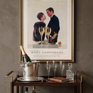 Puede incluir: Un carrito de bar de estilo vintage con un anuncio enmarcado de Mo&euml;t Champagne. El carrito contiene una botella de champ&aacute;n en una cubitera, copas de champ&aacute;n y botellas de licor. Tambi&eacute;n hay un libro y una jarra.