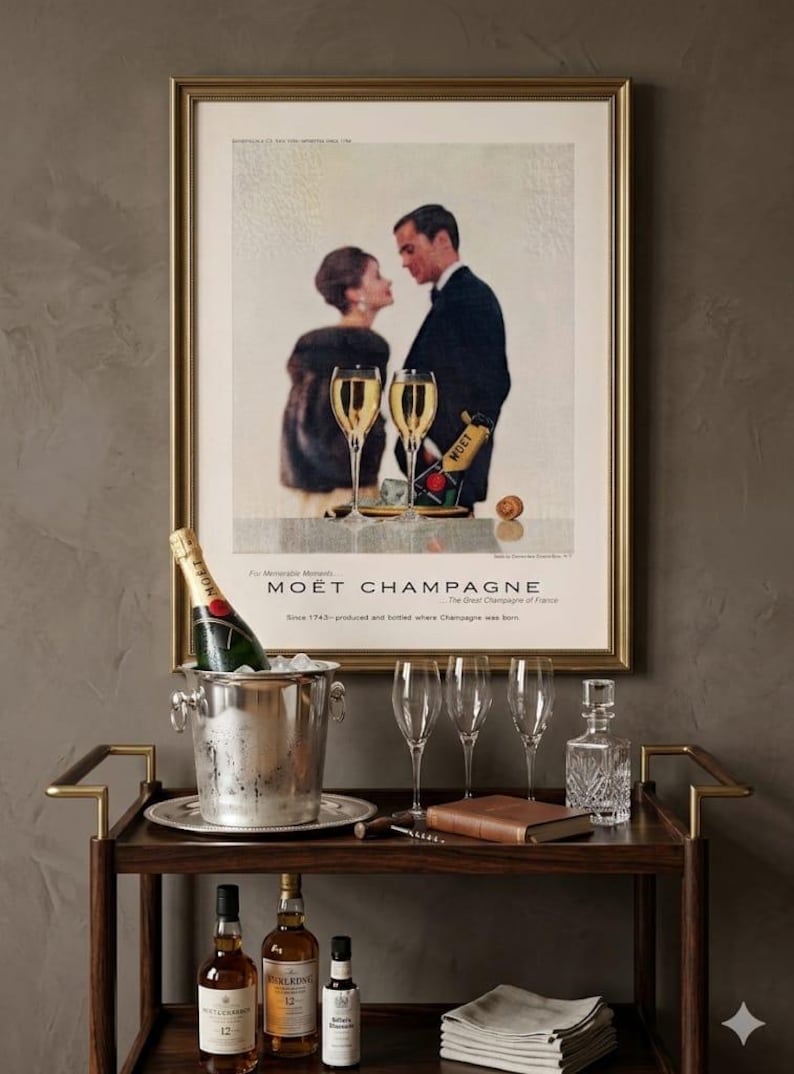 Puede incluir: Un carrito de bar de estilo vintage con un anuncio enmarcado de Mo&euml;t Champagne. El carrito contiene una botella de champ&aacute;n en una cubitera, copas de champ&aacute;n y botellas de licor. Tambi&eacute;n hay un libro y una jarra.