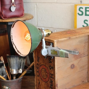 May include: A vintage green metal desk lamp with a distressed finish. The lamp has a brass fitting and a light bulb. The lamp is mounted on a wooden box. The lamp is a unique piece of industrial decor.