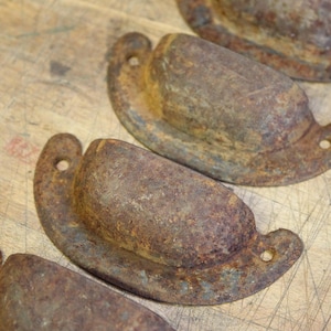 May include: Four rusty metal drawer pulls with a rounded, oval shape. The pulls have a distressed, aged look and are perfect for adding a vintage touch to furniture.