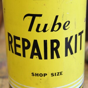 以下が含まれることがあります： 黒い文字で「Tube REPAIR KIT」と書かれた黄色のチューブ修理キット。「SHOP SIZE」の文字も含まれています。少し使い込まれたような、ヴィンテージ感のある外観です。