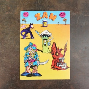 May include: A colorful illustration with the word "ZAM" at the top. The image features cartoon characters, including a pirate, a tree-like figure, and a red griffin with an ink bottle. The background is yellow with palm trees and a blue sky.