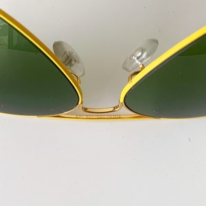 Puede incluir: Gafas de sol aviador amarillas y doradas con lentes verdes. Las gafas tienen el logotipo de Ray-Ban en el lateral.