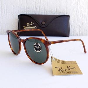 Puede incluir: Gafas de sol Ray-Ban carey con lentes verdes, un estuche de cuero marr&oacute;n y una etiqueta que dice "Ray-Ban" y "Constant Density Lenses". Las gafas de sol tienen una montura redonda cl&aacute;sica.