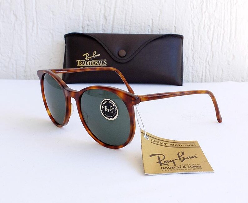 Puede incluir: Gafas de sol Ray-Ban carey con lentes verdes, un estuche de cuero marr&oacute;n y una etiqueta que dice "Ray-Ban" y "Constant Density Lenses". Las gafas de sol tienen una montura redonda cl&aacute;sica.