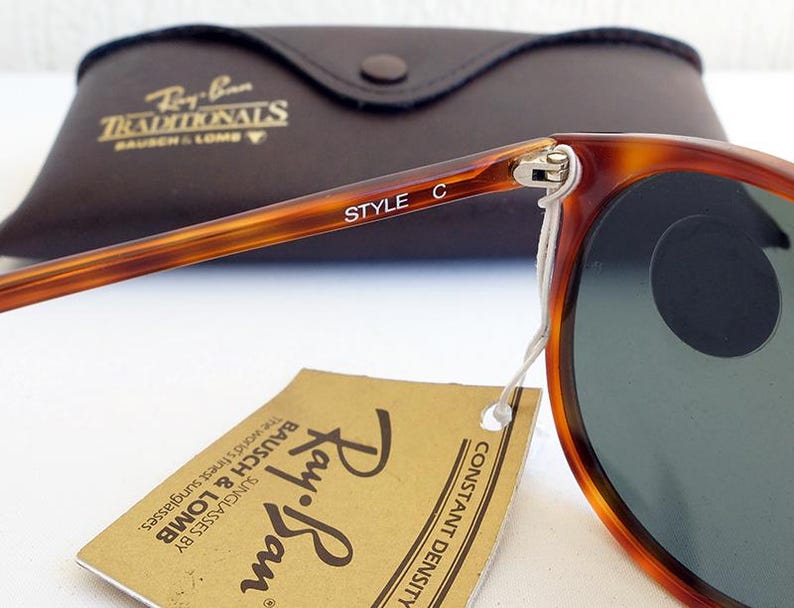Puede incluir: Primer plano de gafas de sol Ray-Ban con montura carey y lentes verdes. Las palabras "STYLE C" est&aacute;n impresas en la patilla. Tambi&eacute;n se ve un estuche de cuero marr&oacute;n y una etiqueta con el logotipo de Ray-Ban.