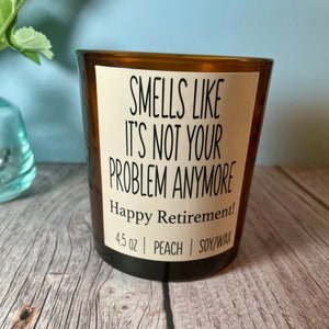 May include: A brown glass candle with a white label that reads "Smells like it's not your problem anymore! Happy Retirement!"  The candle is 4.5 ounces, peach scented, and made with soy wax.