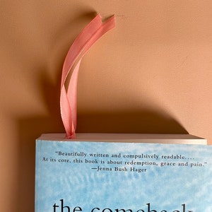 May include: A book titled "The Comeback" with a light blue cover and a pink ribbon bookmark. The book cover features a quote from Jenna Bush Hager: "Beautifully written and compulsively readable... At its core, this book is about redemption, grace and pain."