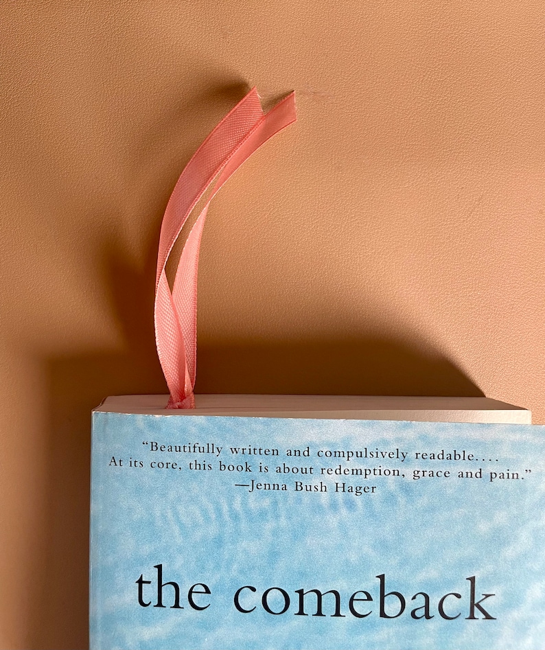 May include: A book titled "The Comeback" with a light blue cover and a pink ribbon bookmark. The book cover features a quote from Jenna Bush Hager: "Beautifully written and compulsively readable... At its core, this book is about redemption, grace and pain."