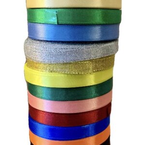 May include: A stack of 15 different colored satin ribbon rolls. The colors include silver, navy blue, purple, cream, green, blue, gray, gold, yellow, dark green, pink, burgundy, blue, orange, black, white, and pink.