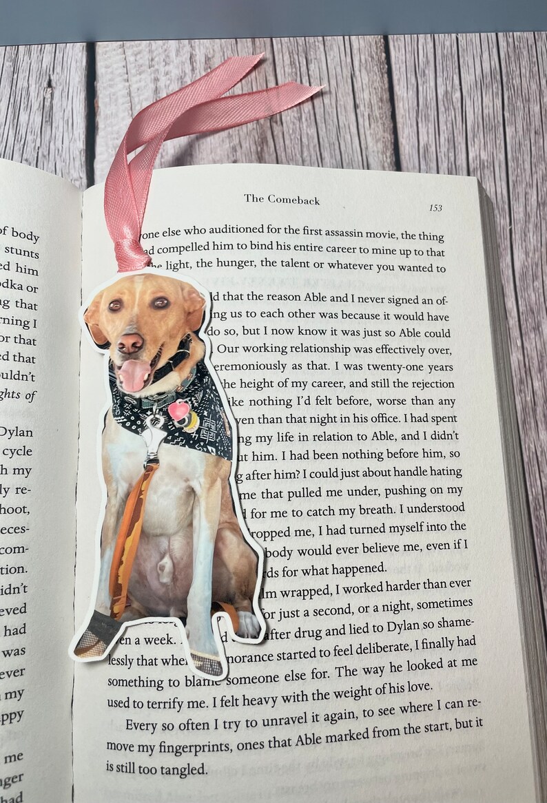 May include: A bookmark featuring a brown and white dog with a bandana. The bookmark is shaped like the dog and is made of a sturdy material. The bookmark is placed on a page of a book with the text "The Comeback" visible.