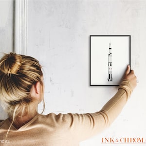 May include: A black framed print of a white and gray rocket ship on a white wall. The print is 8x10 inches and is hanging vertically.