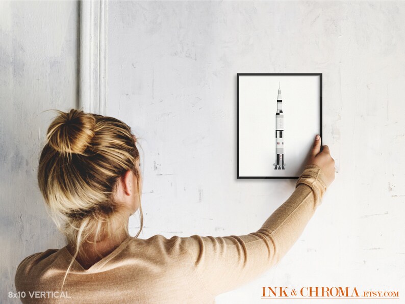 May include: A black framed print of a white and gray rocket ship on a white wall. The print is 8x10 inches and is hanging vertically.