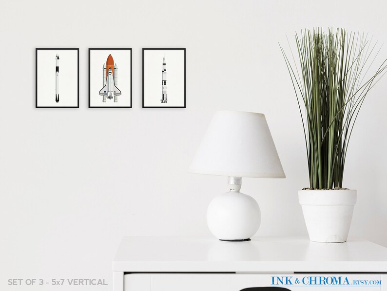 May include: Set of three black and white illustrations of rockets and space shuttles. The illustrations are framed and displayed on a white wall. The frames are 5x7 inches.