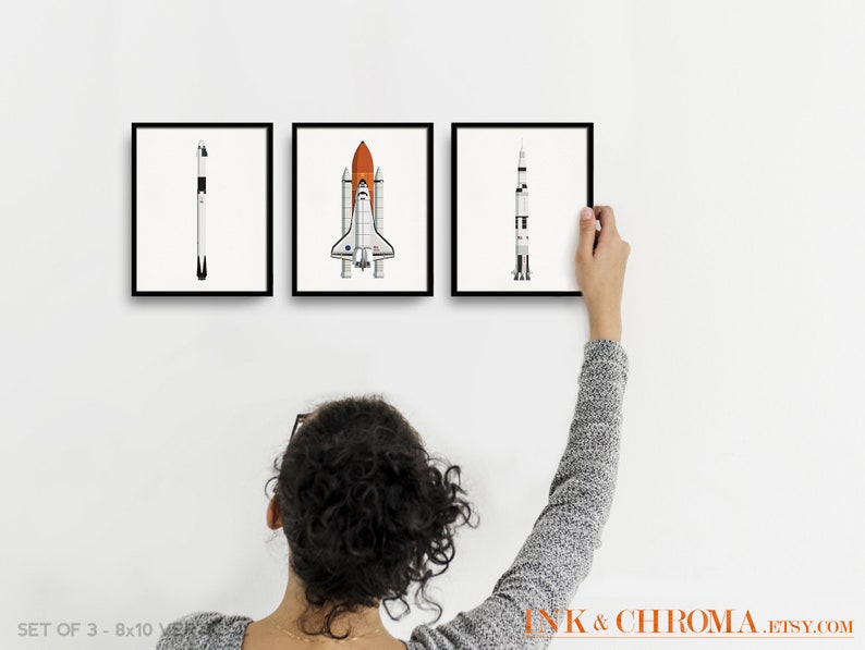 May include: Set of three black framed prints featuring illustrations of different types of rockets. The prints are hanging on a white wall. The prints are 8x10 inches.