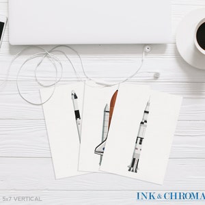 May include: Set of three 5x7 inch vertical prints featuring illustrations of different spacecrafts, including a space shuttle, a rocket, and a capsule. The prints are on white paper and have a minimalist design.