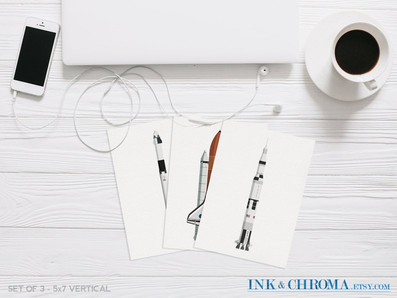 May include: Set of three 5x7 inch vertical prints featuring illustrations of different spacecrafts, including a space shuttle, a rocket, and a capsule. The prints are on white paper and have a minimalist design.