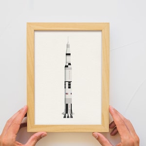 May include: A framed print of a white and black rocket ship with a red, white, and blue American flag on the side. The rocket ship is on a white background.