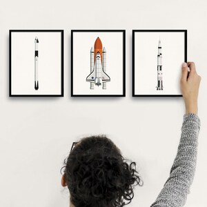 May include: Three framed illustrations of spacecrafts, including a space shuttle, a rocket, and a satellite. The illustrations are in a minimalist style with white backgrounds and black outlines.