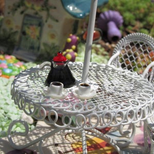 Peut inclure: Une table en m&eacute;tal blanc avec une chaise en m&eacute;tal blanc. Il y a une cafeti&egrave;re miniature et deux tasses de caf&eacute; sur la table. La table et la chaise sont d&eacute;cor&eacute;es d'un motif d&eacute;licat et complexe.
