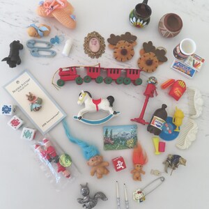 May include: A collection of miniature toys and trinkets, including a red toy train, a rocking horse, a framed portrait, and several small dolls. Other items include a baby bottle, dice, and a Hello Kitty pin.