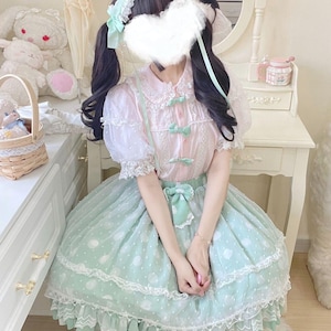 May include: A pastel pink and mint green Lolita dress. The dress features a white lace collar, puff sleeves, and a mint green skirt with white polka dots. The outfit is accessorized with a matching headband and bows.