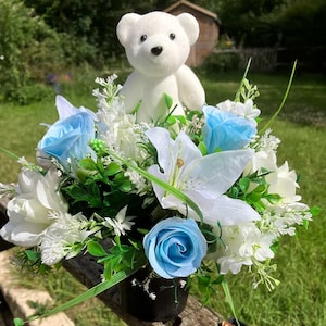 Een kinderherdenkingspot met bloemen citroen en blauw bloemstuk bloemstuk in zwarte plastic pot met een gevlokte teddybeer voor babyjongen