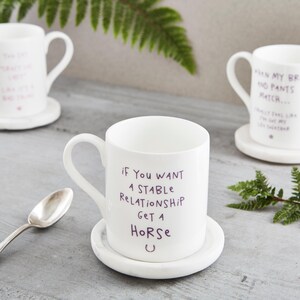 Può includere: Tazze in ceramica bianca con frasi umoristiche in scrittura viola. Una tazza recita: «Se vuoi una relazione stabile, prendi un cavallo». Ogni tazza è su un piattino abbinato.