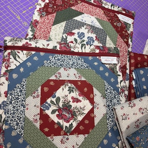 May include: Two quilted fabric pouches with floral patterns in red, blue, green, and white. The pouches have red zippers and a burgundy ribbon. The design features a central diamond shape with a large floral motif.