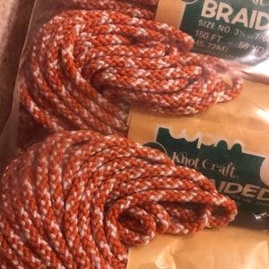 May include: A close-up of orange and white braided cord in a plastic bag. The label reads "Khot Craft Braid Size No. 3 1/2 - 7/64 150 ft. 50 yds."