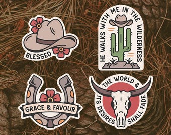 May include: Four Western-themed sticker designs. One shows a cowboy hat with "Blessed", another a cactus with a hat and the text "He walks with me in the wilderness". The other two feature a horseshoe with "Grace & Favour" and a bull skull with "The world & its desires shall fade".