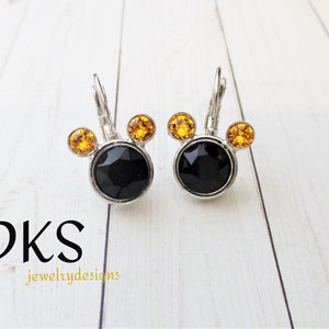 May include: A pair of silver earrings with black and amber rhinestones. The earrings are shaped like Mickey Mouse heads.