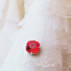 May include: A red square-shaped rhinestone pendant on a clear string necklace.