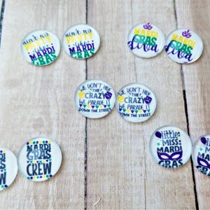 May include: Assortment of Mardi Gras themed glass cabochons with various sayings, including "Ain't no party like a Mardi Gras", "We don't hide the crazy, we parade it down the street", and "Mardi Gras Crew".