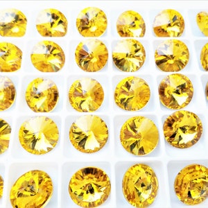May include: A close-up view of a tray of round, yellow, faceted rhinestones. The rhinestones are arranged in a grid pattern and are all the same size.