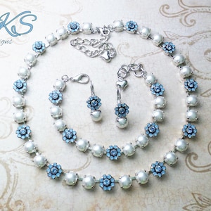 May include: A set of pearl and blue crystal jewelry, including a necklace, bracelet, and earrings. The jewelry is silver-toned and features a delicate floral design.