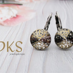 May include: A pair of silver hoop earrings with a round, textured, multi-colored stone in the center. The stone has a black, white, and gold color scheme.